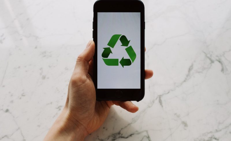 From above view of faceless person holding mobile phone with white screen and green recycle logo above marble surface