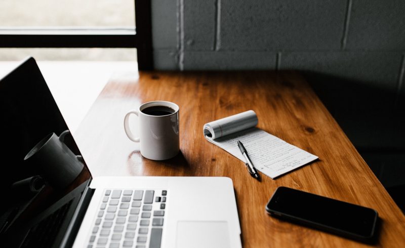 MacBook Pro, white ceramic mug,and black smartphone on table